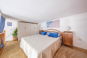 Un dormitorio con cama, cabecero de madera, mesitas de noche, un armario y una planta en maceta.