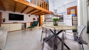 Un vaste espace de vie doté d’un haut plafond, d’un escalier en bois, d’une cuisine équipée d’appareils modernes et d’un coin repas avec des chaises transparentes.