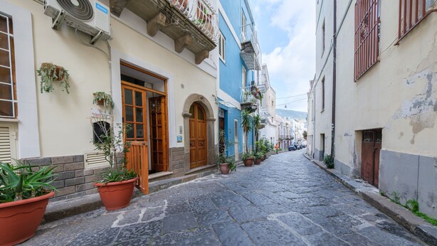 Une ruelle étroite pavée, bordée d’immeubles dotés de portes en arc de cercle et de balcons.