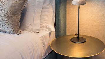 Un lit bien fait, avec du linge de lit blanc et un coussin décoratif, une tête de lit de couleur turquoise et une petite table ronde avec une lampe à côté.