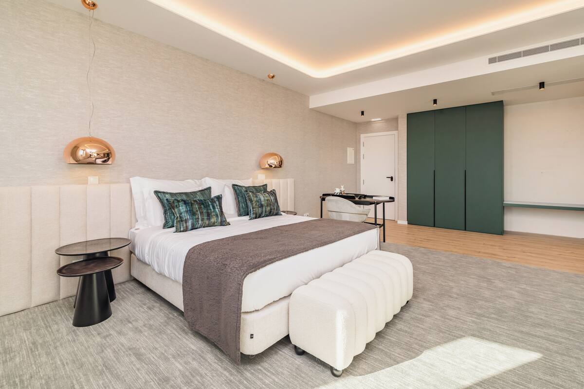 Une chambre à coucher moderne avec un grand lit, des tables de chevet, un banc et une armoire.