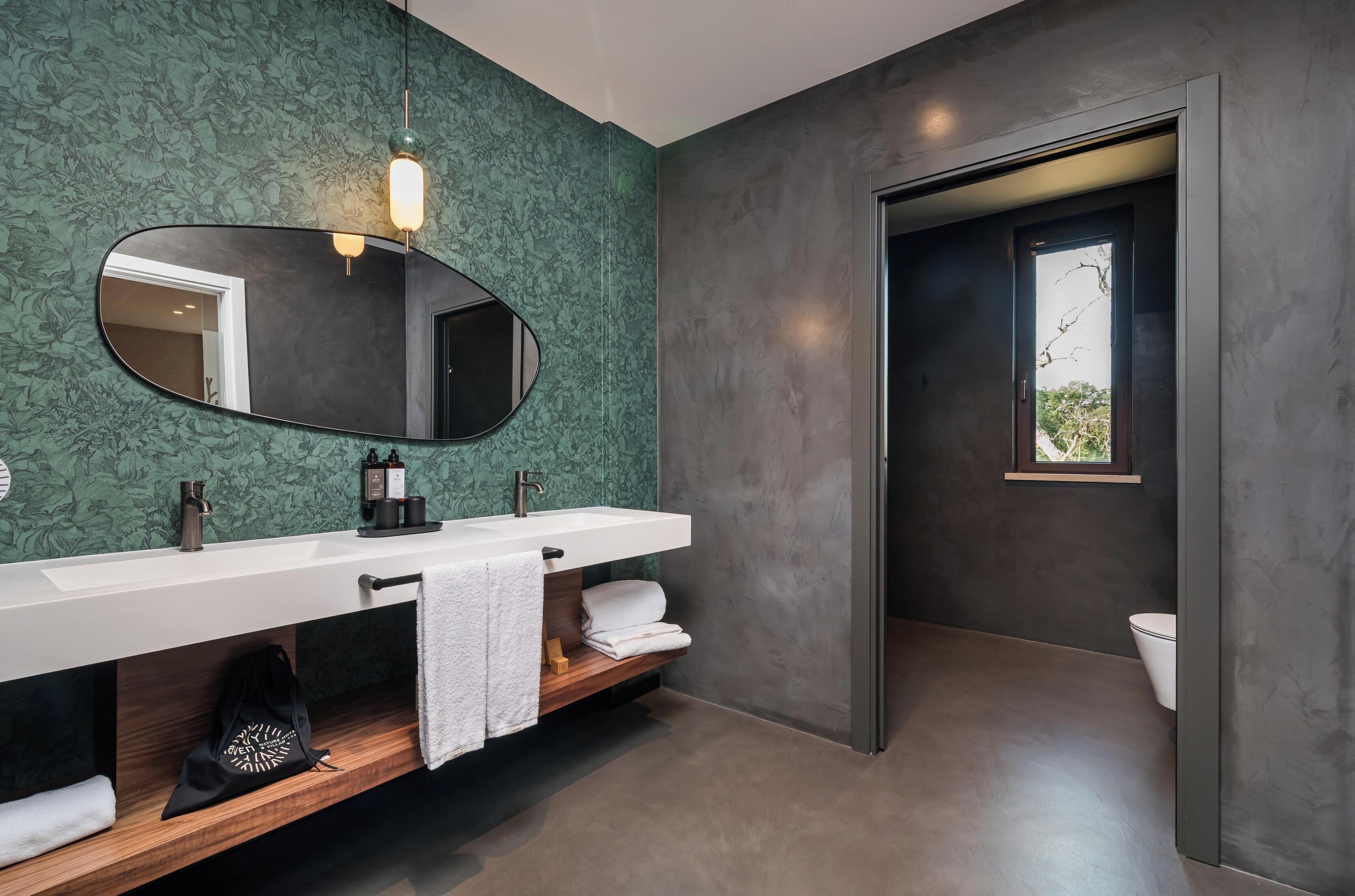 A modern bathroom with a large mirror, two sinks, a towel rack, and a wooden shelf.