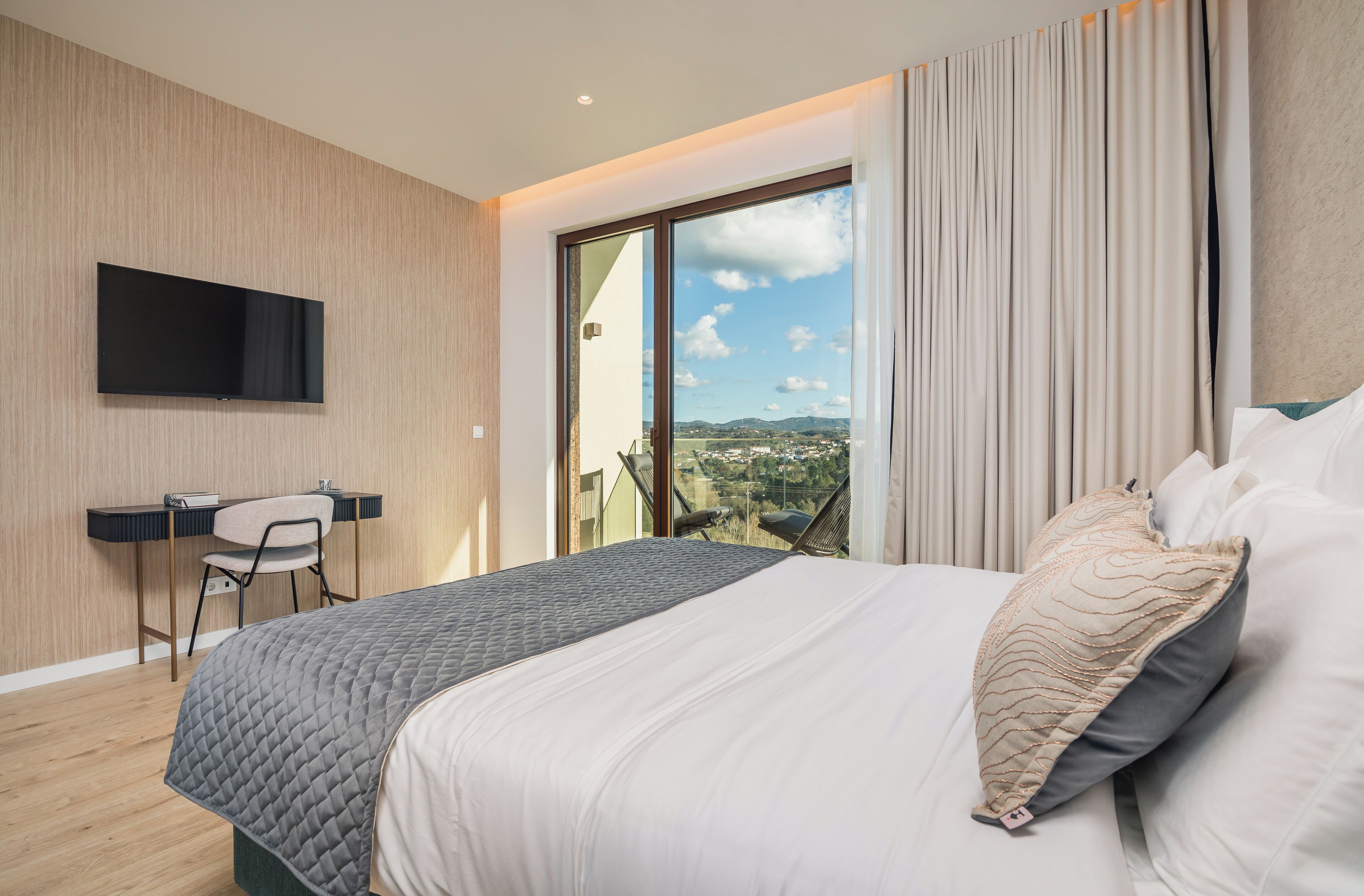 A modern bedroom with a large bed, a desk, and a TV mounted on the wall.