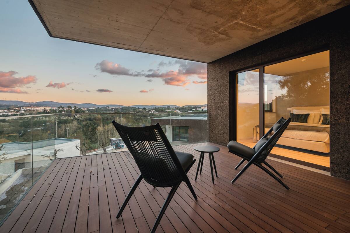 Un balcon doté d’un plancher en bois, de deux chaises noires et d’une petite table ronde.