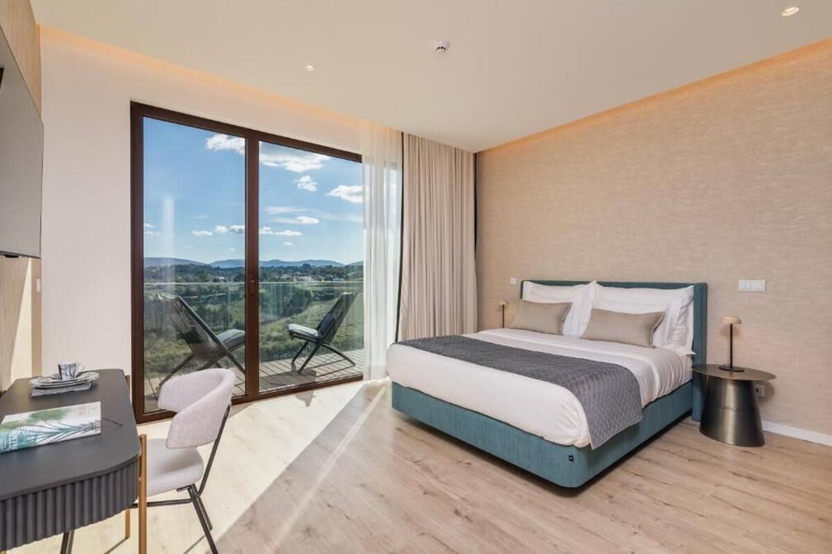 Une chambre d’hôtel moderne dotée d’un grand lit, d’un bureau et d’un balcon offrant une vue sur la campagne.