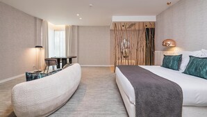Ett modernt hotellrum med en stor säng, en böjd sittgrupp, ett matbord och en dekorativ vägg.