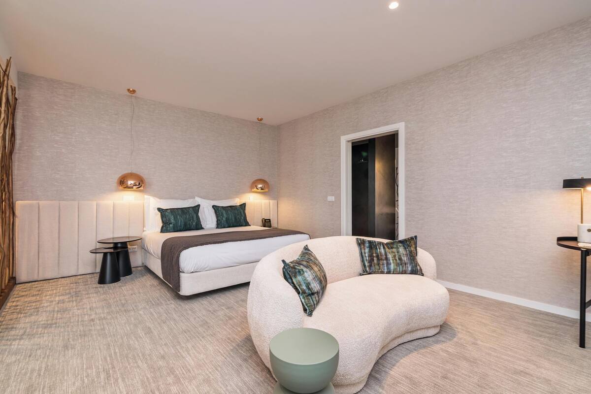 Une chambre à coucher moderne avec un lit, deux tables de chevet, un canapé incurvé et une petite table ronde.
