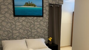 A neatly made bed with a blue bedspread, a framed picture of a beach scene on the wall, and a nightstand with a vase of flowers.