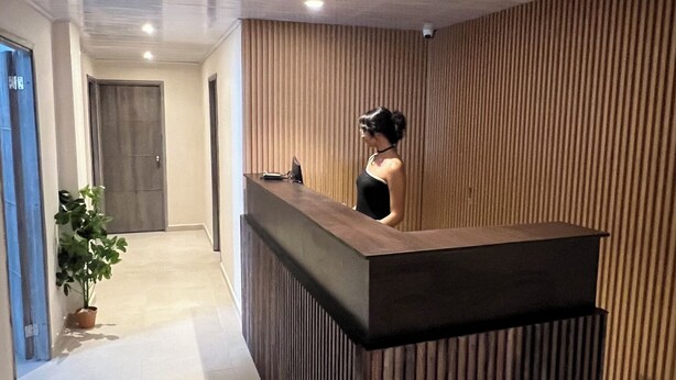A reception area with a wooden reception desk, a potted plant, and a door in the background.