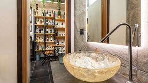 A modern bathroom with a large glass bowl sink, a marble wall, and a wine shelf.