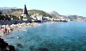 Un pueblo costero con playa, aguas azules cristalinas y una imponente torre de iglesia.