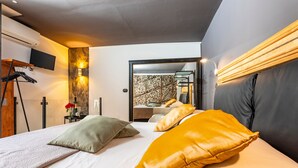 A modern hotel room with a bed, a TV, a mirror, and a staircase leading to an upper floor.