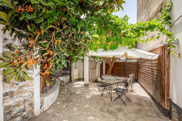 Un patio con una mesa, sillas, un paraguas blanco y un árbol con frutos anaranjados.