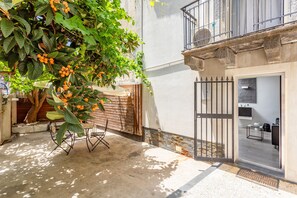A courtyard with a table and chairs, a tree with orange fruits, a gate, and a building with a balcony.