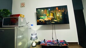 Un salon avec un téléviseur fixé au mur, un four à micro-ondes, une lampe et une télécommande posés sur une table en bois.