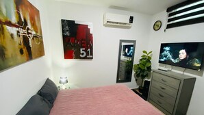 Une chambre avec un lit, une télévision, une commode, une plante et des œuvres d’art murales.