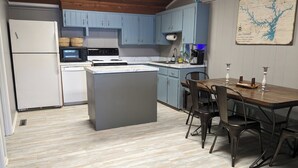 Een keuken met blauwe kastjes, een witte koelkast, een fornuis en een eethoek met een tafel en stoelen.