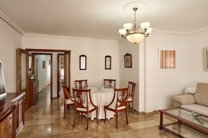 A dining area with a round table, chairs, a chandelier, and a sofa.