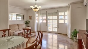A spacious living area with a glass dining table, wooden chairs, a sofa, and a chandelier.