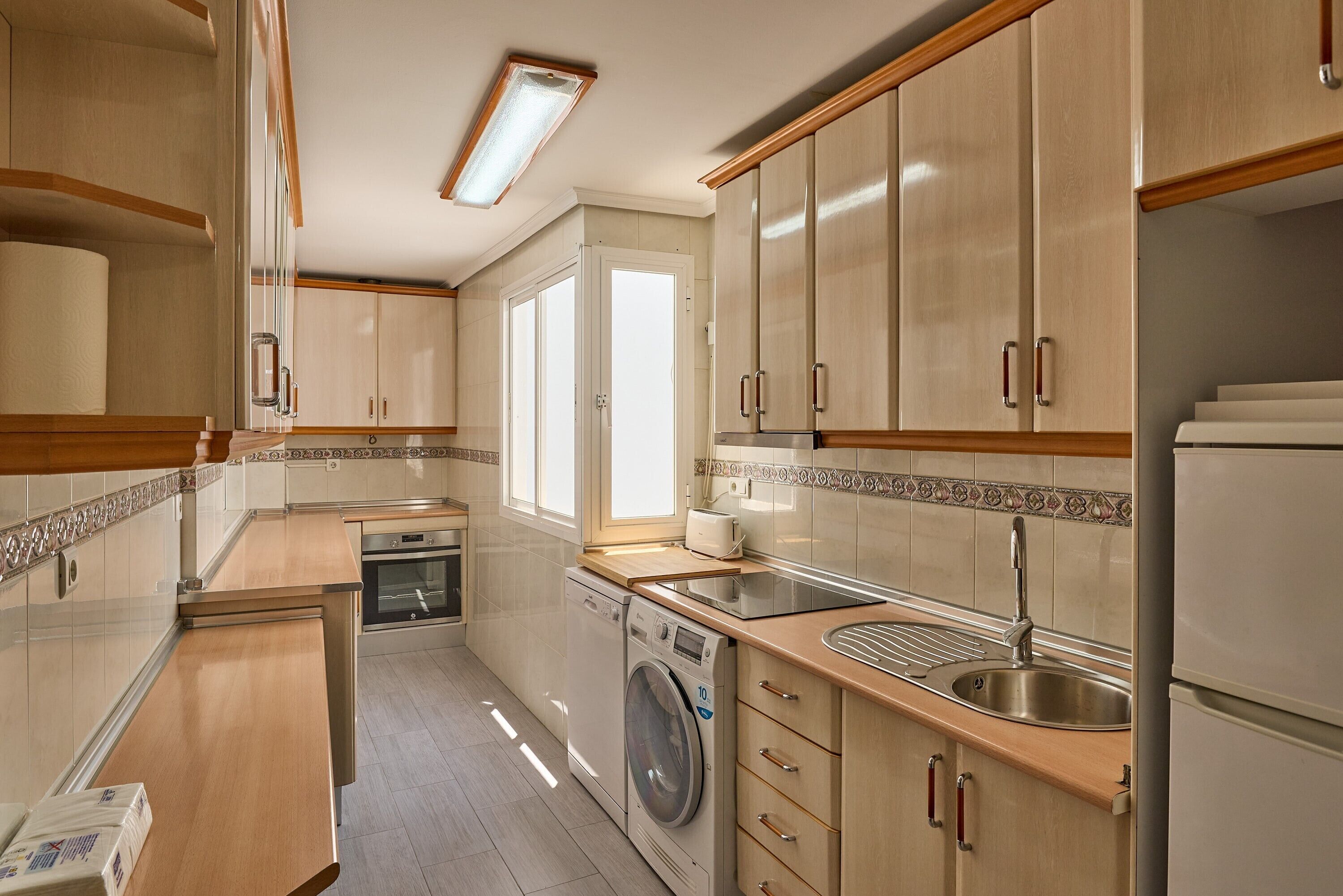 A compact kitchen with a washing machine, a sink, and wooden cabinets.