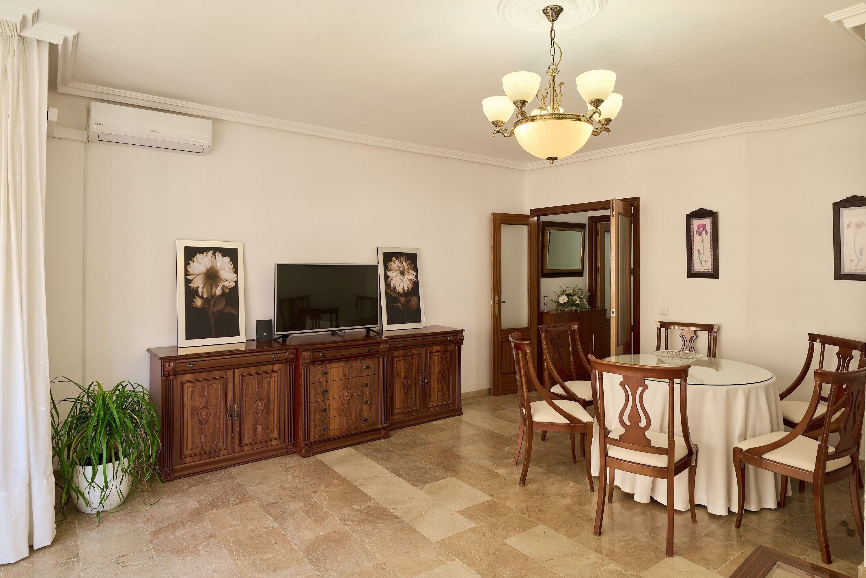 A dining area with a round table, chairs, a television on a wooden cabinet, and framed pictures on the wall.