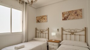 A bedroom with two single beds, a nightstand with a lamp, and two wall-mounted paintings.