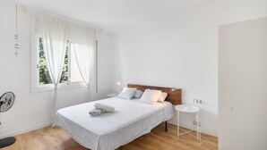 A bedroom with a bed, bedside table, and a standing fan. - Apartment 'Fantastic Beach' with Balcony, Wi-Fi and Air Conditioning (Alella)
