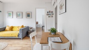A modern living room with a sofa, a dining table with chairs, and a kitchen area in the background. - Apartment 'Fantastic Beach' with Balcony, Wi-Fi and Air Conditioning (Alella)