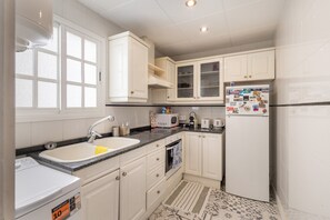 A kitchen with white cabinets, a sink, a microwave, a refrigerator, and a patterned rug.