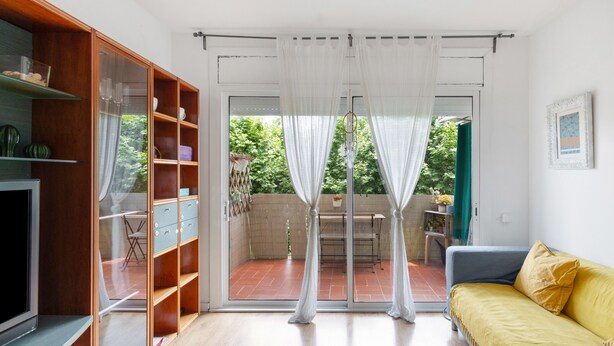 A room with a sliding glass door leading to a patio, a sofa, a TV, and a wooden cabinet with shelves. - Apartment 'Fantastic Beach' with Balcony, Wi-Fi and Air Conditioning (Alella)