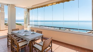 A balcony with a table set for dining, large windows with a view of the sea, and a tiled floor. - Apartment 'Panoramic Sea Views' with Sea View, Wi-Fi and Air Conditioning (Manilva)