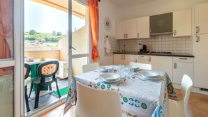 A kitchen with white cabinets, a tiled backsplash, and a dining area with a table set for two. - Vacation Home 'Mare Nostrum' with Mountain View, Private Terrace, and Air Conditioning (Castelsardo)