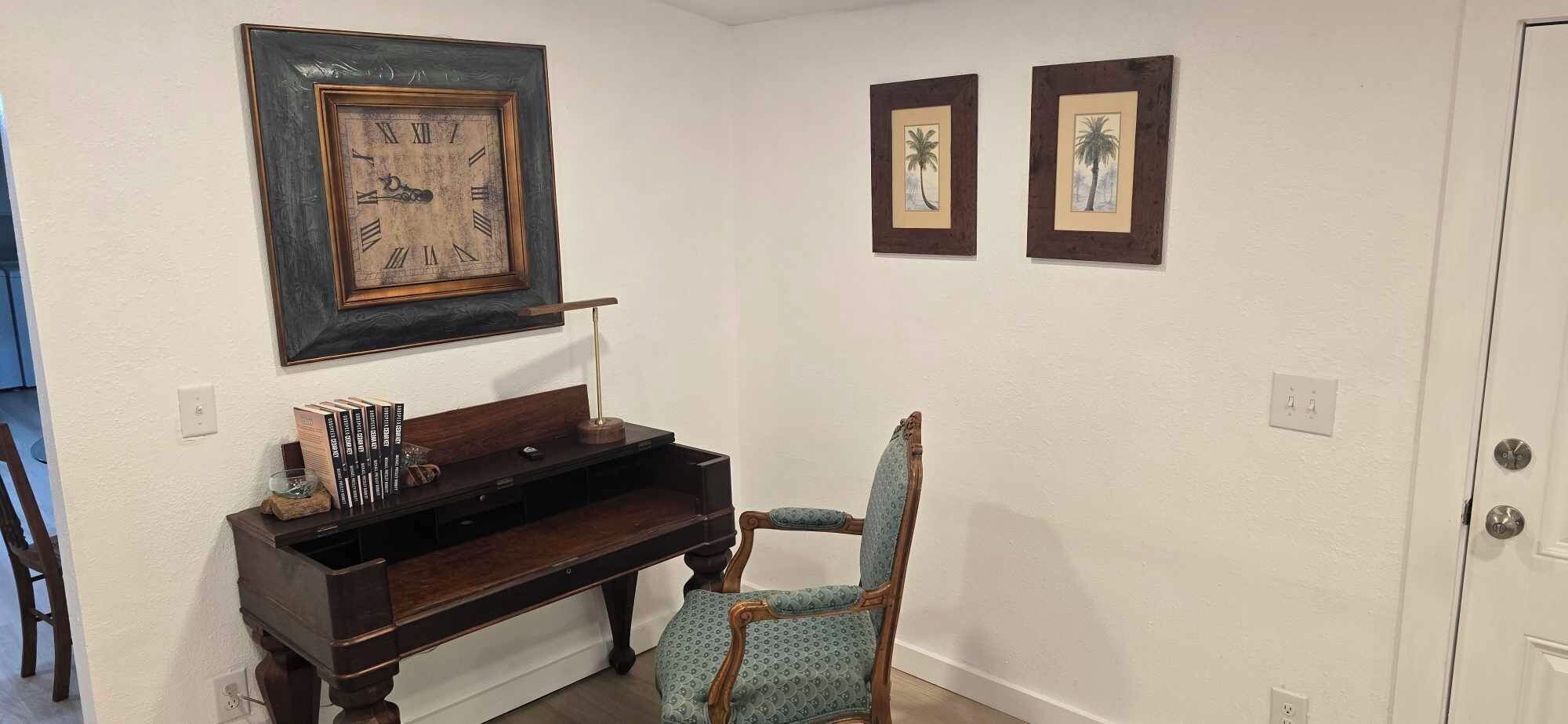 Une pièce avec un piano, une chaise et deux tableaux encadrés accrochés au mur.