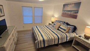A bedroom with a bed, bedside lamps, a TV, and a window. - Clambassador Cottage (Cedar Key)