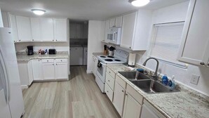 A compact kitchen with white cabinets, a built-in microwave, a stove, and a sink. - Clambassador Cottage (Cedar Key)