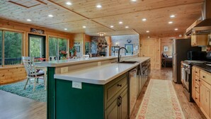 A spacious kitchen with wooden cabinets, a central island, and a large window overlooking a deck. - County Highway - Trail Access, Lake Access, Sleeps 23 (Minong)