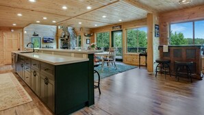 A spacious kitchen with a large island, wooden cabinets, and a stone fireplace. There is a dining area with a table and chairs, and a bar area with stools. - County Highway - Trail Access, Lake Access, Sleeps 23 (Minong)