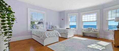 A bedroom with two beds, a large window, and a view of the sea.