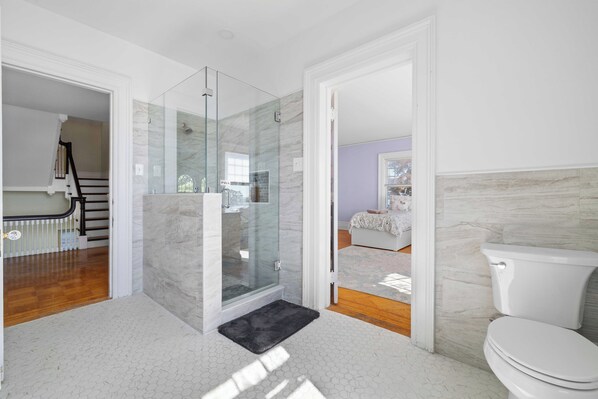 A modern bathroom with a glass shower enclosure, a white toilet, and a visible staircase leading to another room. - Waterfront Estate in Groton – 10 Bedrooms, Private Pier, & Beach Access (Groton)