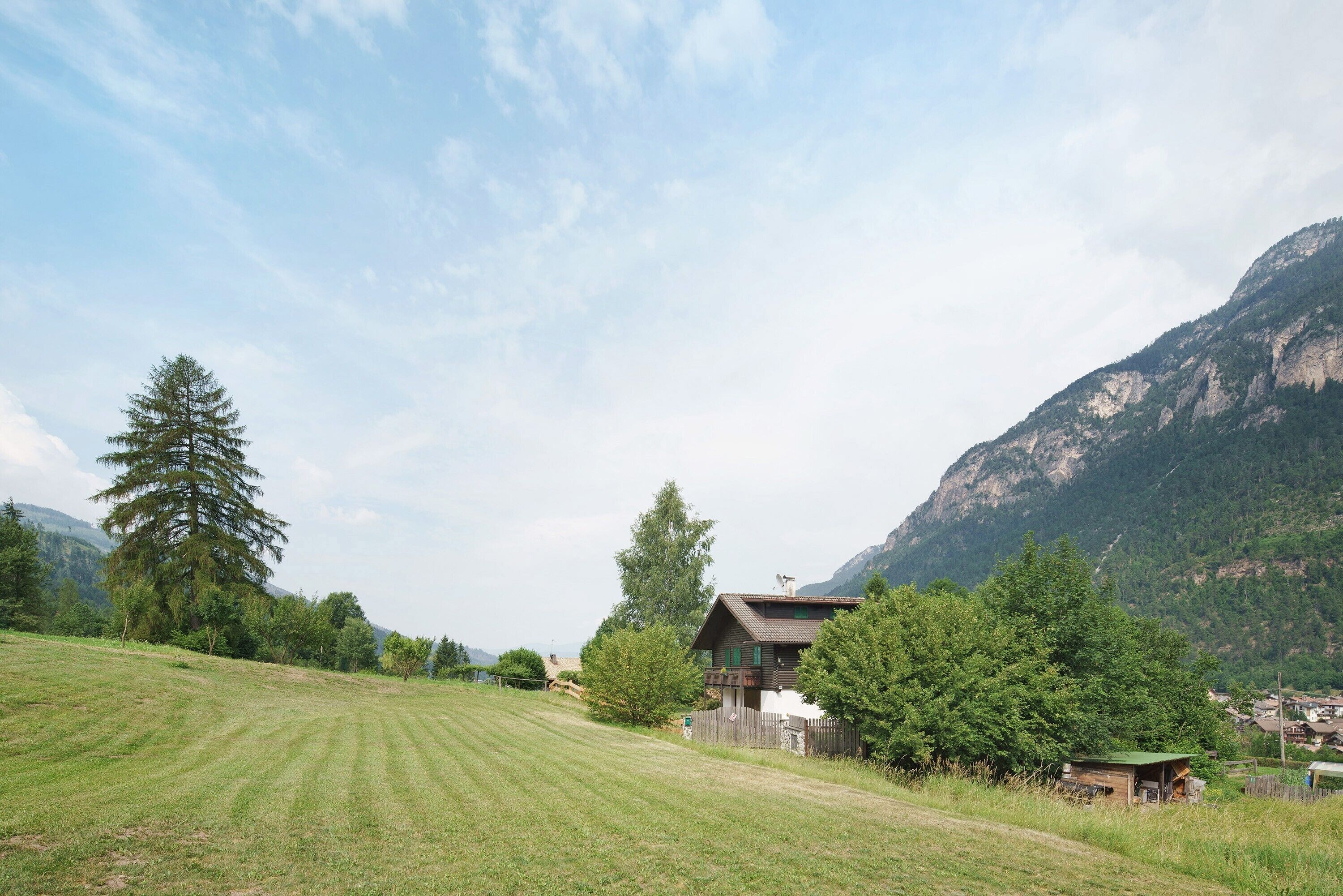 Ländliche Landschaft mit einem Haus, einem Feld und Bergen im Hintergrund.