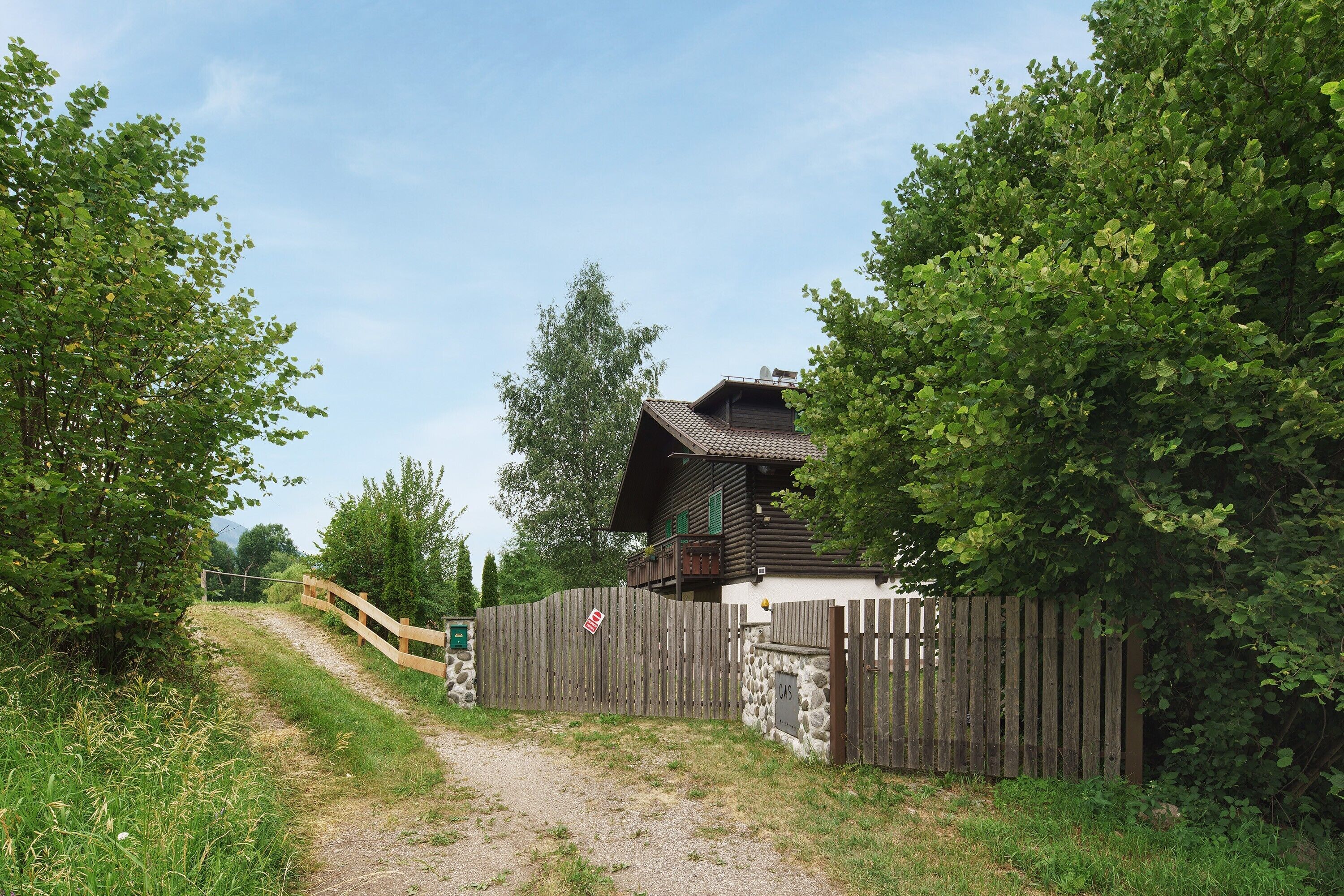 A wooden house with a stone foundation, a wooden fence, and a gravel path leading to the entrance.
