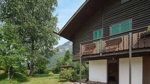 Un chalet en bois doté d’un balcon, entouré de verdure et de montagnes.
