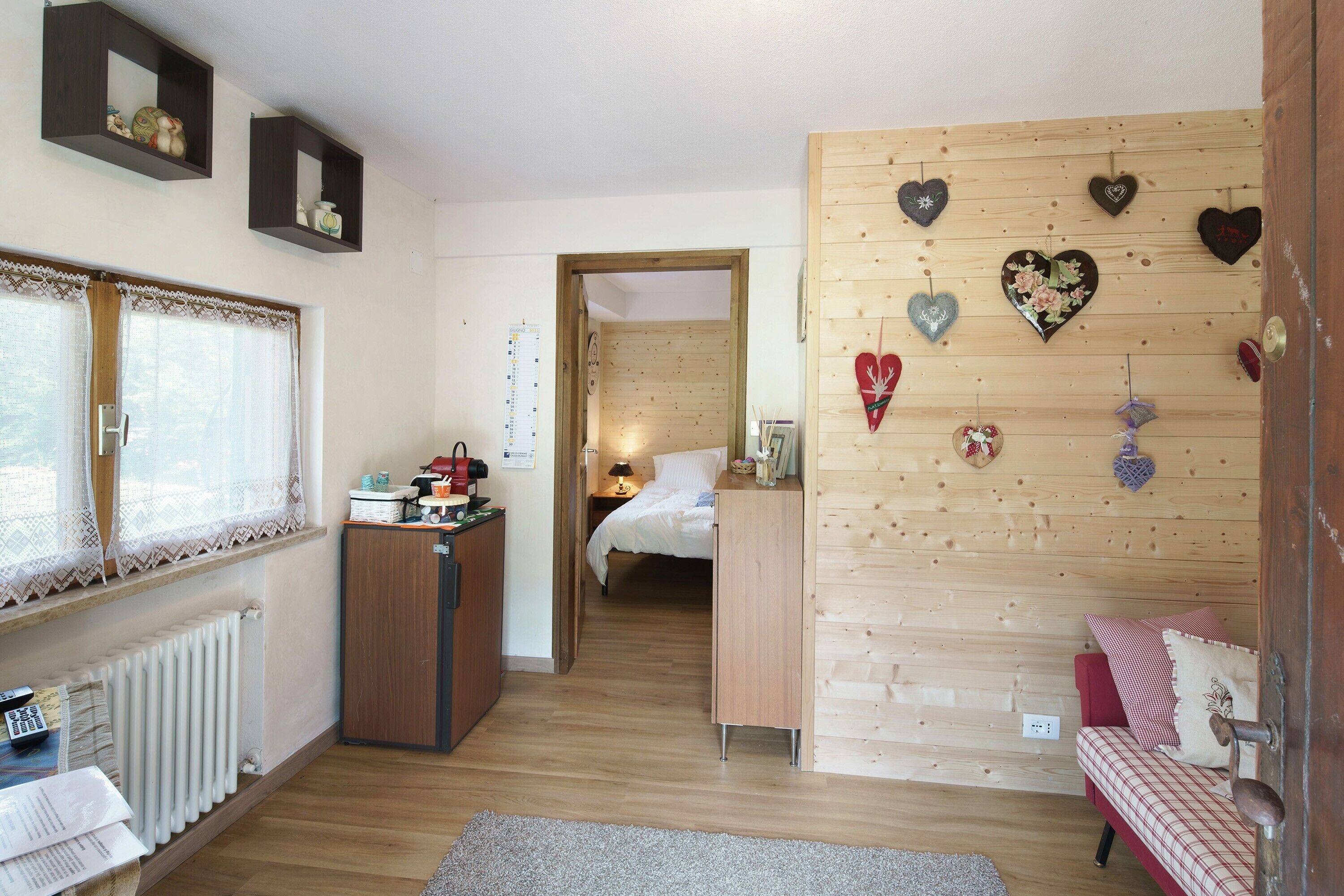 A cozy room with a wooden floor, a bed with a red and white checkered bedspread, a wooden dresser, and a wall decorated with heart-shaped ornaments.