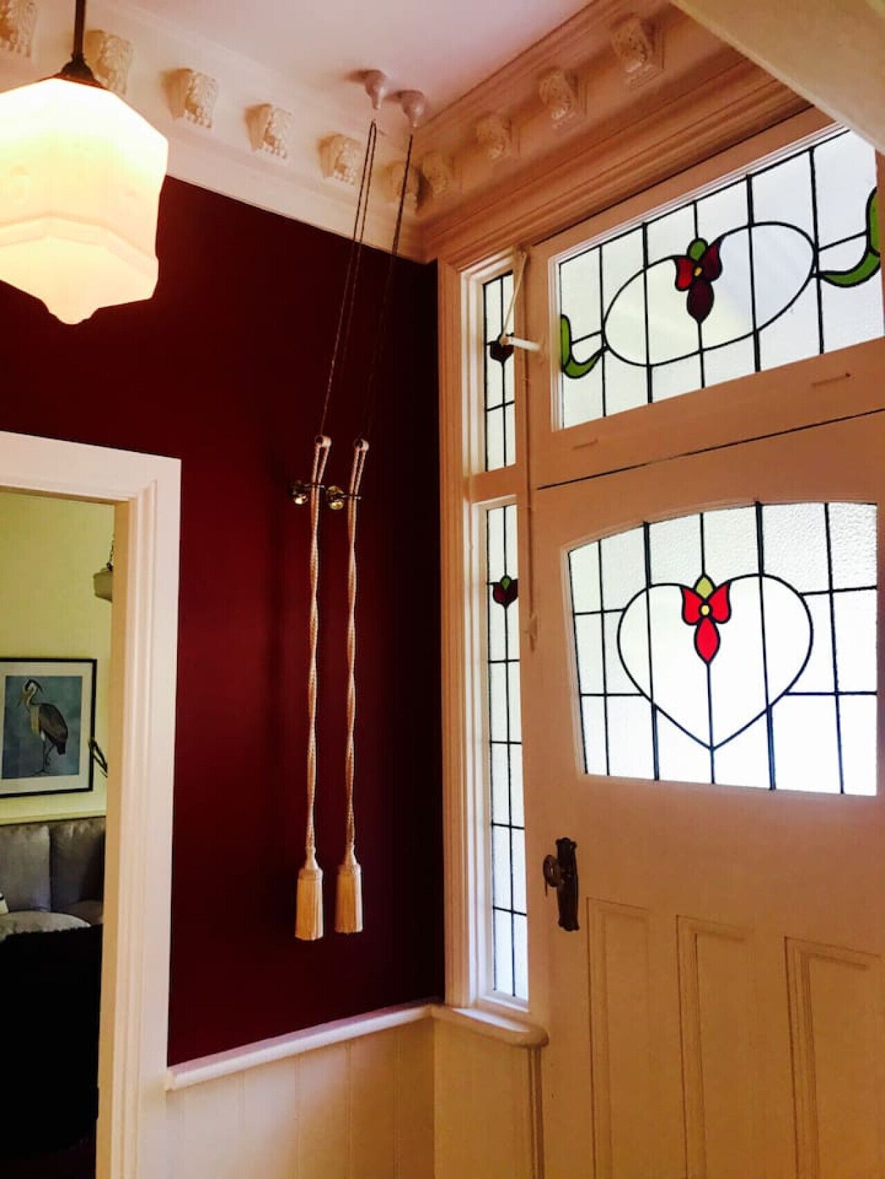 A room with a red wall, a white door with stained glass, and a hanging light fixture.