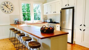 A kitchen with a central island, bar stools, a stainless steel refrigerator, and a clock on the wall.