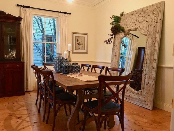 Un comedor con una mesa y sillas de madera, un armario y un espejo grande.