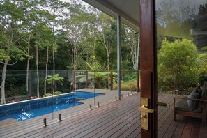 A wooden deck with a pool, surrounded by lush greenery and trees.