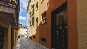 Une ruelle étroite pavée, bordée d’immeubles dotés de balcons, et une grande porte vitrée sur le côté droit.