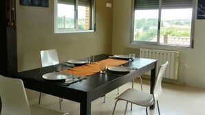 Zona de menjador amb taula negra, cadires blanques i vistes a verdura a través de les finestres.