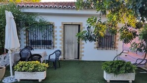 Zona de pati amb una paret blanca, dues finestres amb reixes metàl·liques, una porta i dos testos amb vegetació.